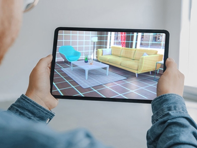 Decorating Apartment: Man Holding Digital Tablet with AR Interior Design Software Chooses 3D Furniture for Home. Man is Choosing Sofa, Table for Living Room. Over Shoulder Screen Shot with 3D Render